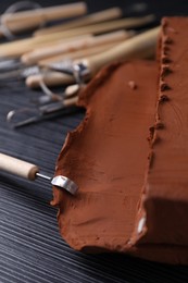 Photo of Clay and modeling tool on dark gray wooden table, closeup