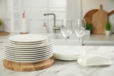 Photo of Clean plates, glasses and butter dish on white marble table in kitchen