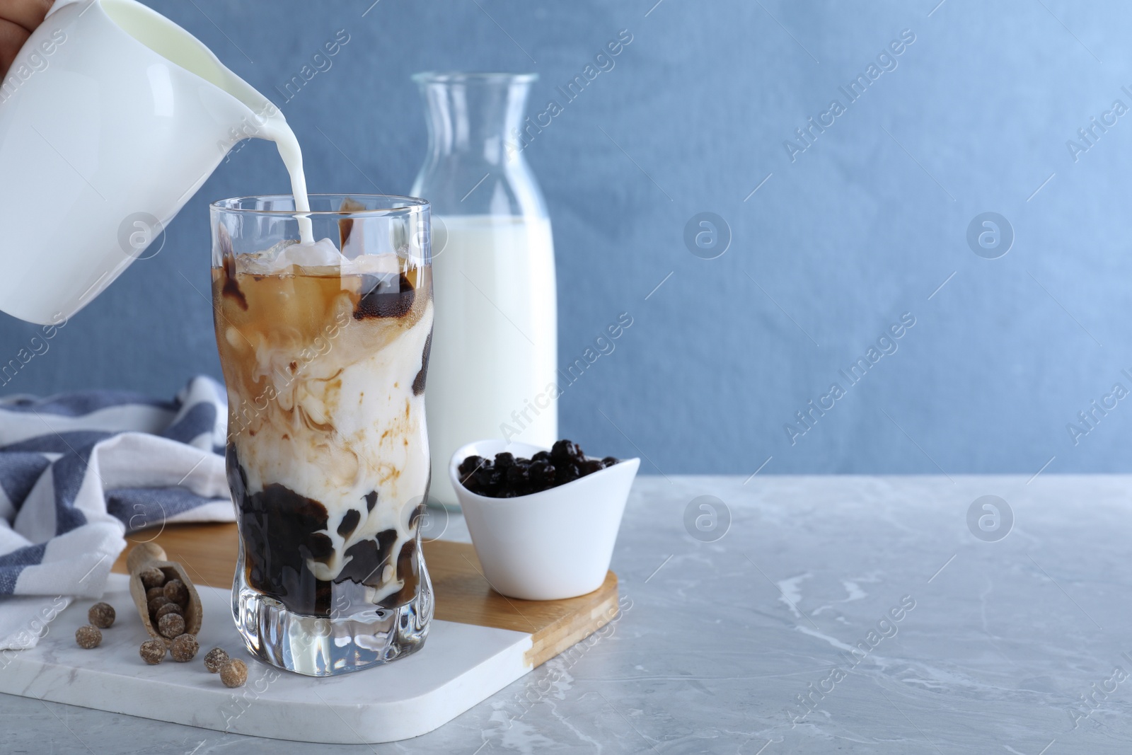 Photo of Person preparing bubble milk tea with tapioca balls at grey marble table against blue background. Space for text