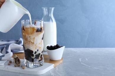 Person preparing bubble milk tea with tapioca balls at grey marble table against blue background. Space for text