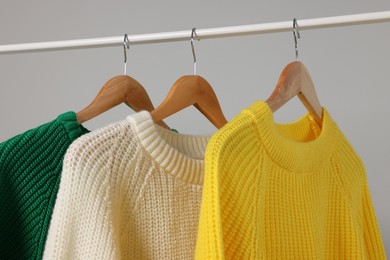 Rack with different warm sweaters on light grey background