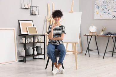 Photo of Young woman with brush palette near easel in studio