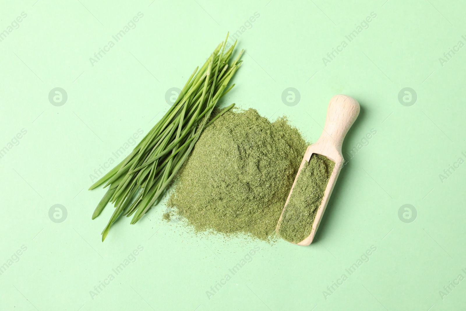Photo of Pile of wheat grass powder, scoop and fresh sprouts on green table, flat lay