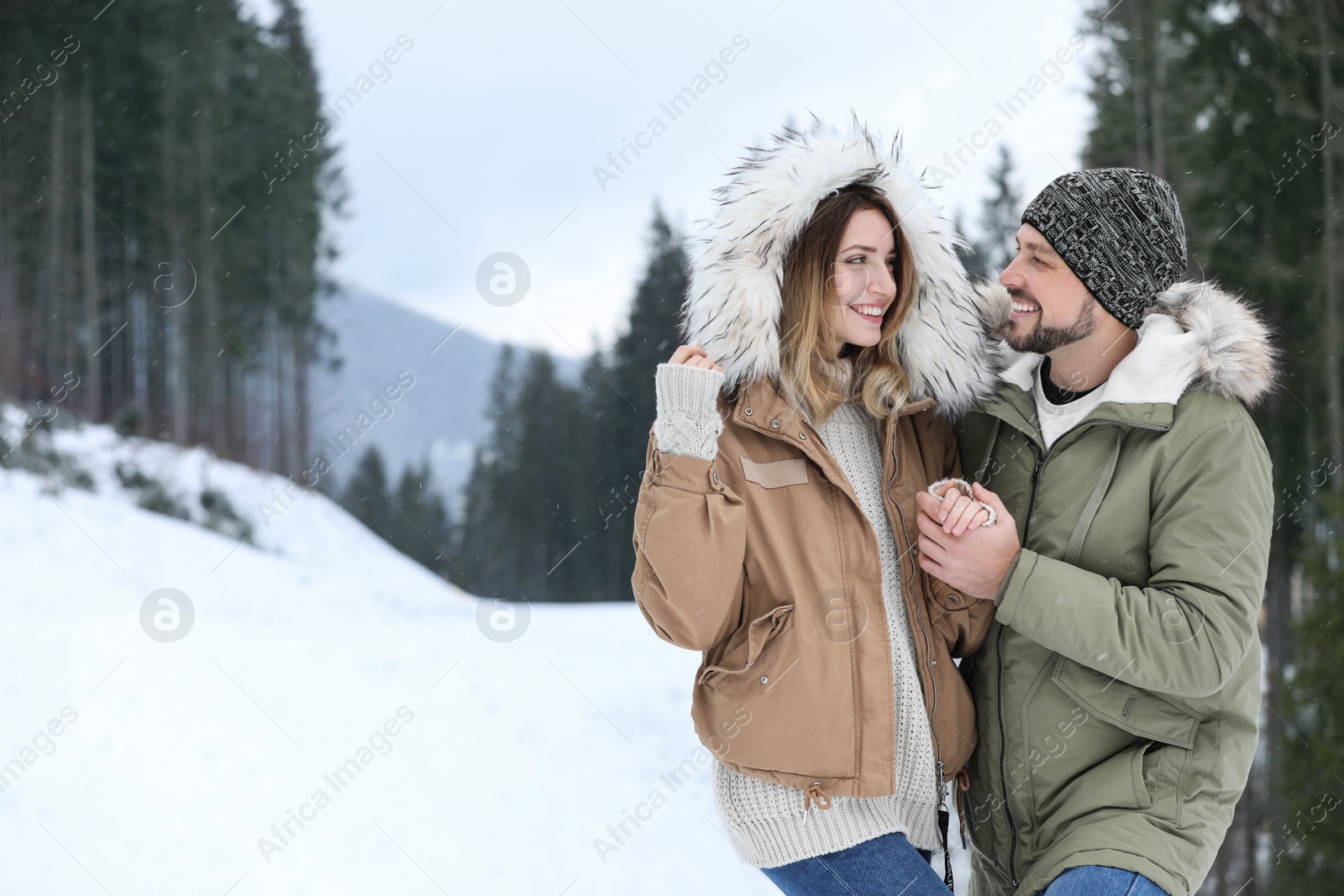 Photo of Happy couple near conifer forest on snowy day, space for text. Winter vacation