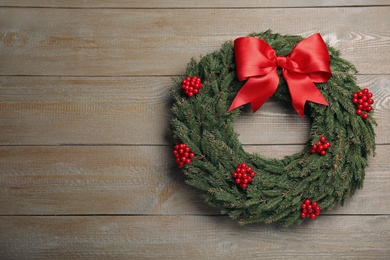 Photo of Beautiful Christmas wreath with red berries and bow on wooden background. Space for text