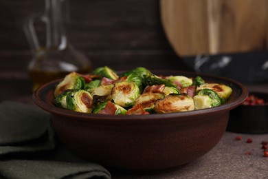 Photo of Delicious roasted Brussels sprouts and bacon in bowl on brown table, closeup