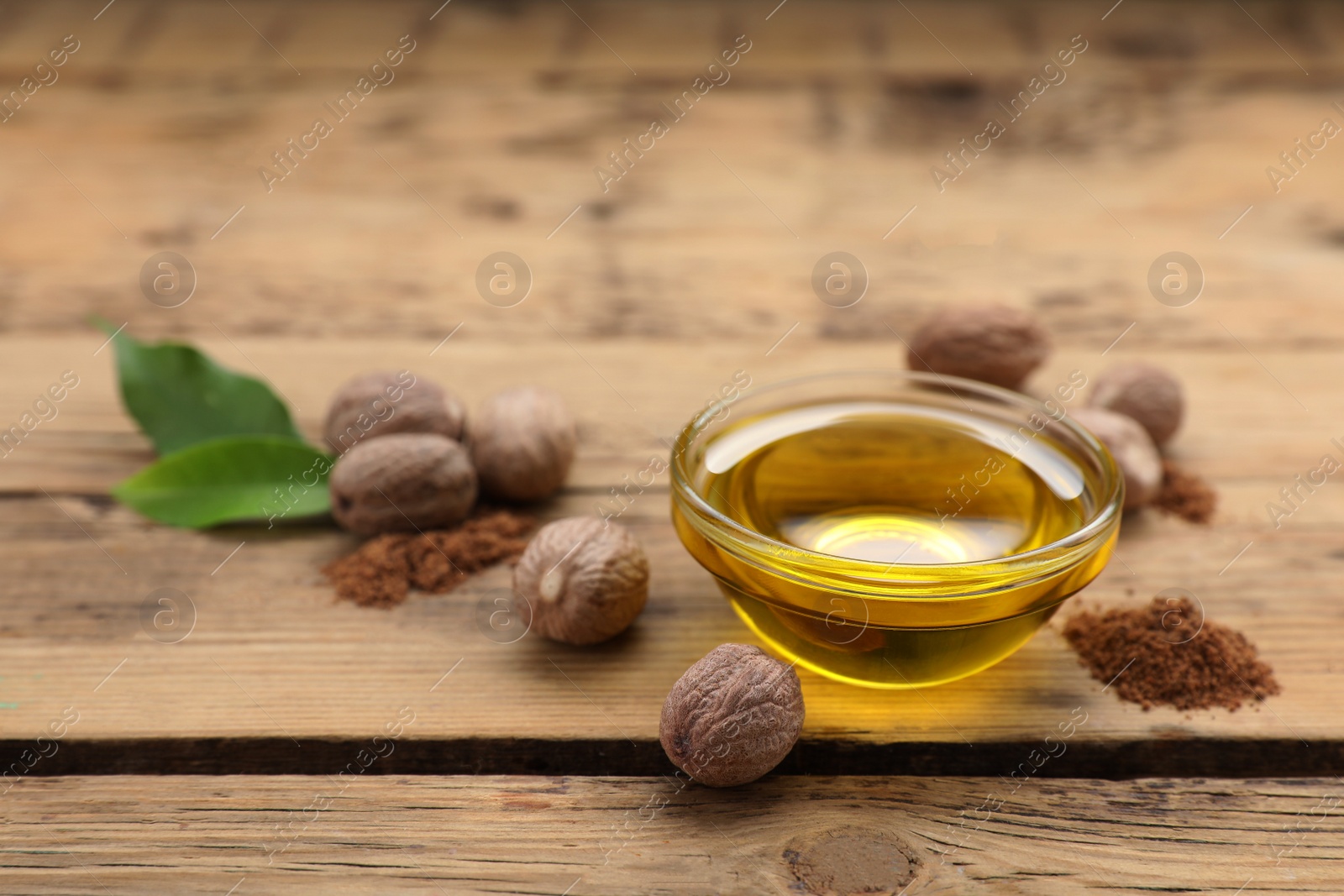Photo of Bowl of nutmeg oil, nuts and powder on wooden table. Space for text