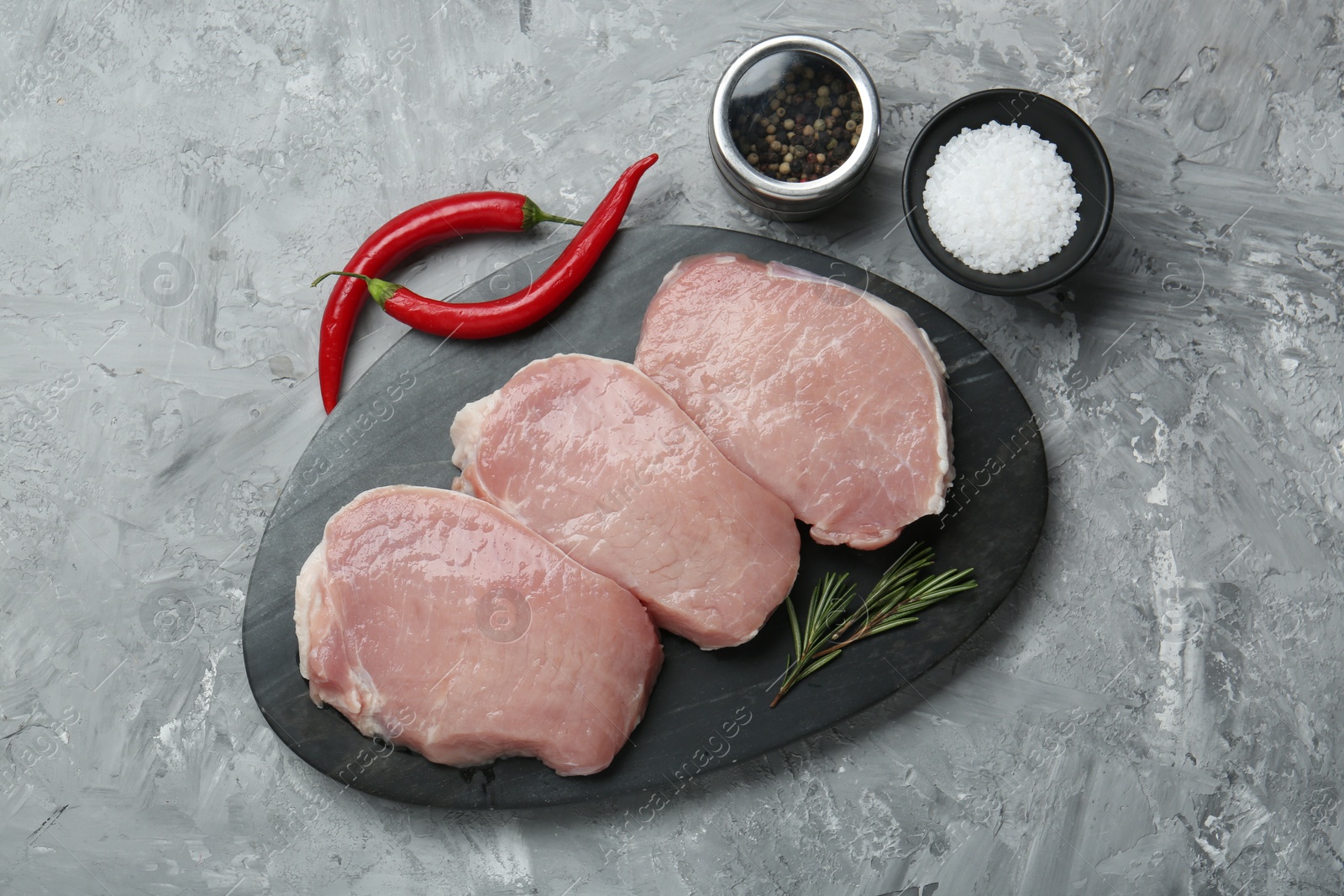 Photo of Pieces of raw pork meat, chili peppers and spices on grey textured table, flat lay