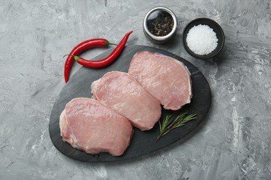 Photo of Pieces of raw pork meat, chili peppers and spices on grey textured table, flat lay