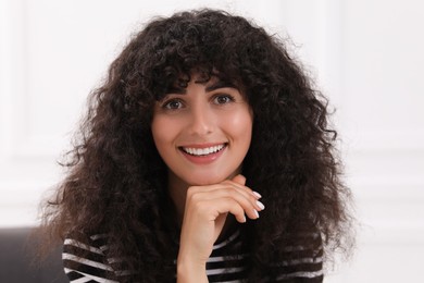 Portrait of beautiful woman with curly hair indoors. Attractive lady smiling and looking at camera