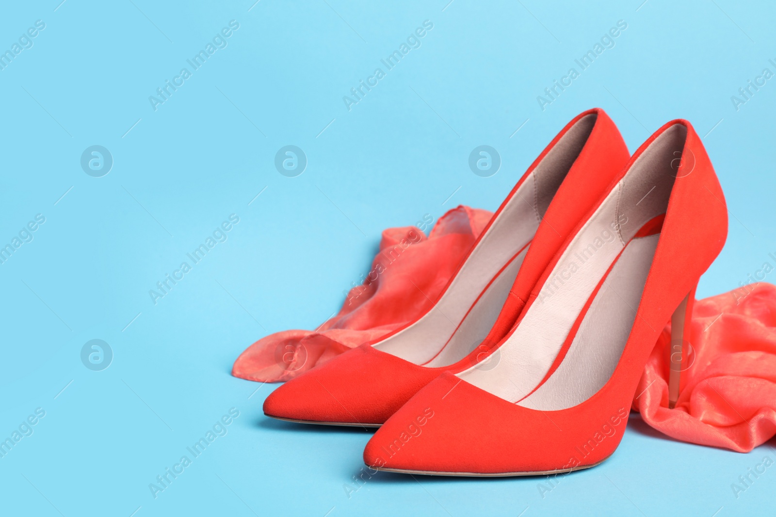 Photo of Stylish coral female shoes and scarf on light blue background. Space for text