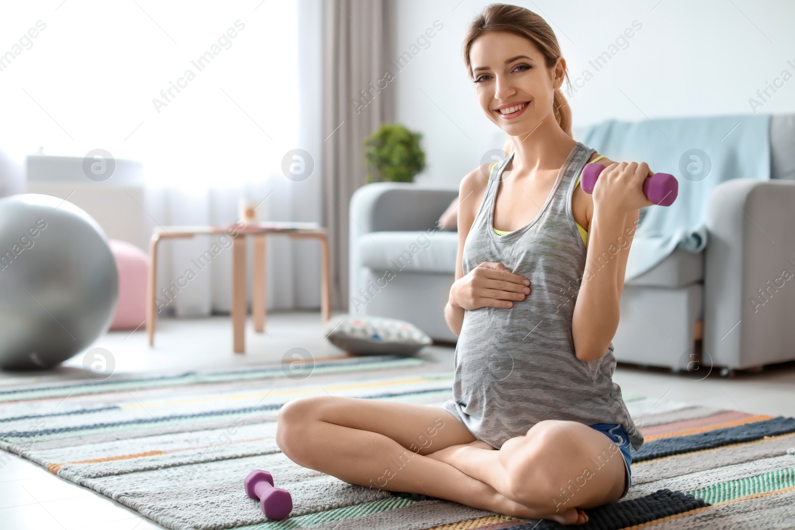 Photo of Young pregnant woman doing exercises with dumbbell at home