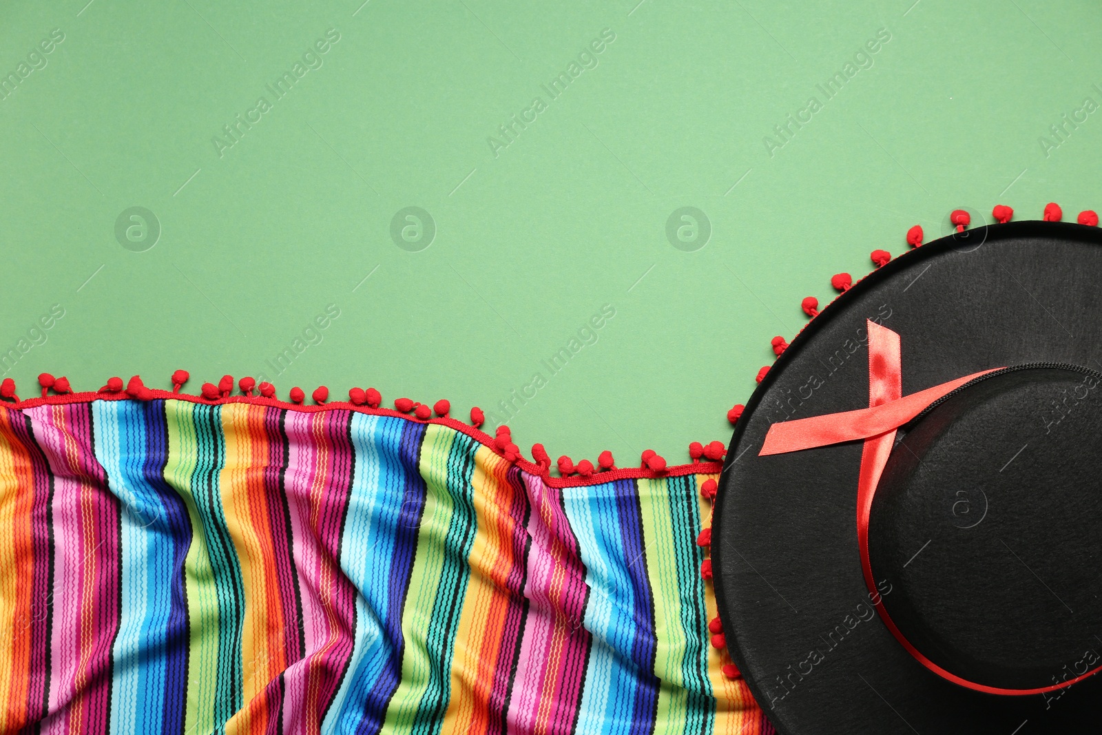 Photo of Mexican sombrero hat and colorful poncho on green background, flat lay. Space for text