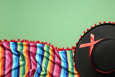Photo of Mexican sombrero hat and colorful poncho on green background, flat lay. Space for text
