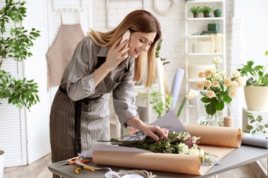 Photo of Female florist talking on phone while making bouquet at workplace
