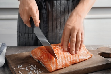 Photo of Woman cutting raw salmon fillet on wooden board