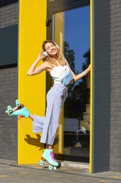 Happy girl with retro roller skates standing near glass door