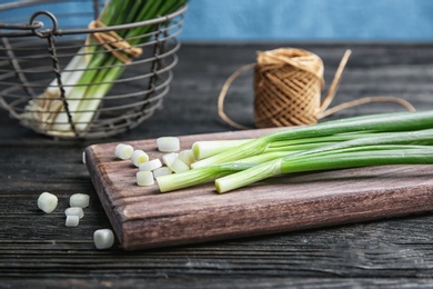 Photo of Wooden board with fresh green onion on table