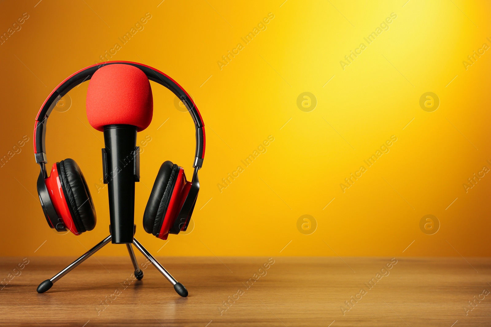 Photo of Microphone and modern headphones on wooden table against orange background, space for text