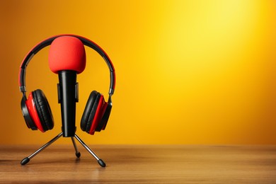 Microphone and modern headphones on wooden table against orange background, space for text