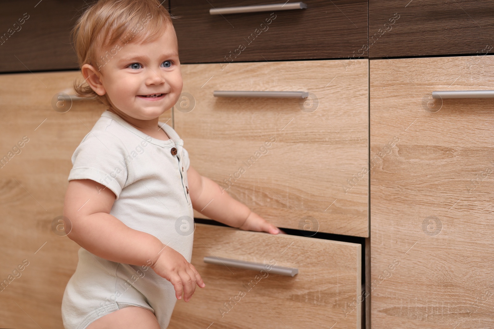 Photo of Little child exploring drawer indoors. Dangerous situation