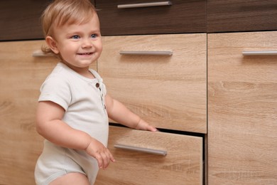 Photo of Little child exploring drawer indoors. Dangerous situation
