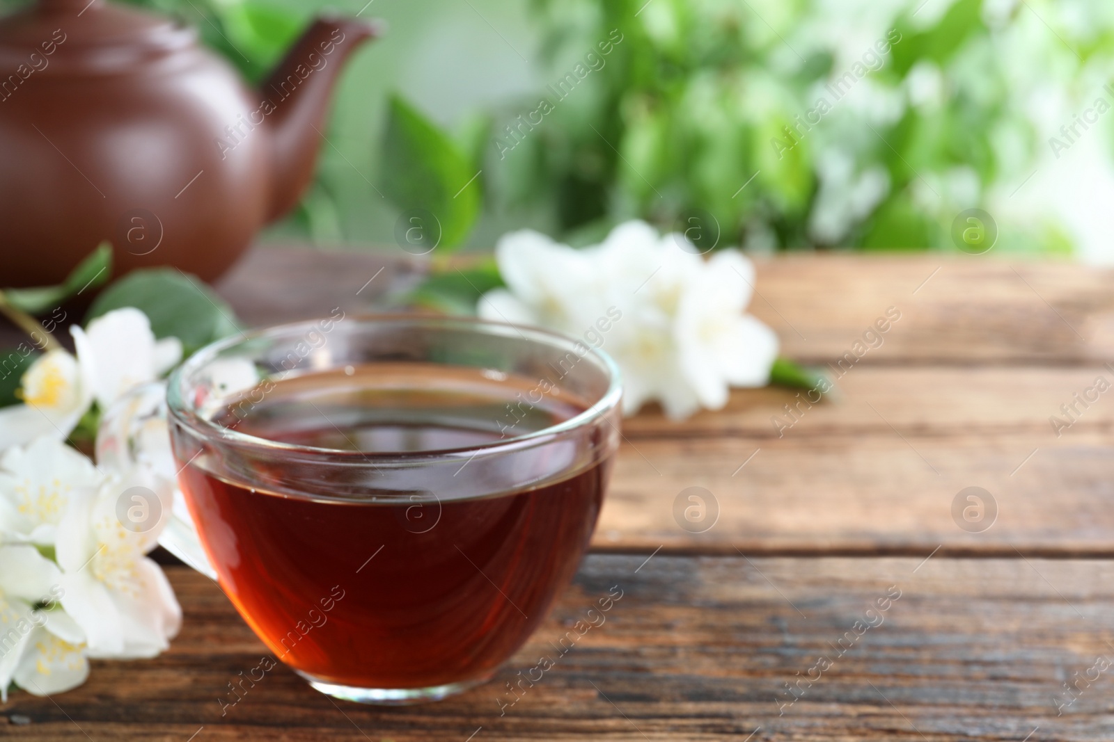 Photo of Cup of tea and fresh jasmine flowers on wooden table. Space for text