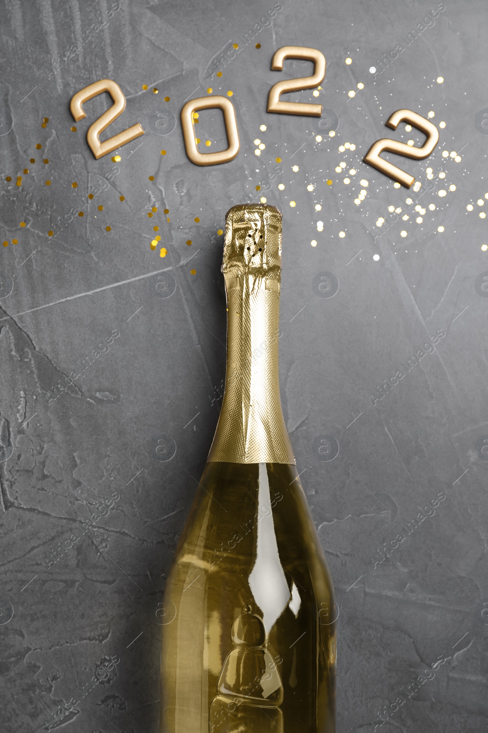Photo of Bottle of sparkling wine, gold confetti and number 2022 on grey background, flat lay. Happy New Year