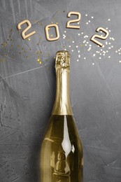 Bottle of sparkling wine, gold confetti and number 2022 on grey background, flat lay. Happy New Year