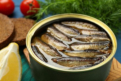 Tin can with tasty sprats and products on table, closeup