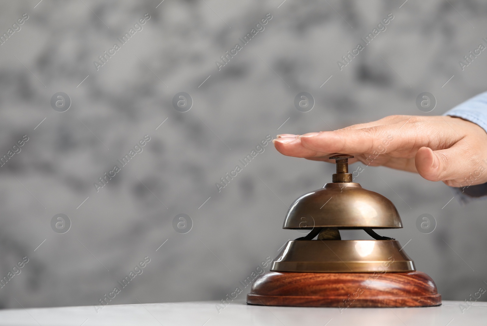 Photo of Woman ringing hotel service bell on grey background. Space for text