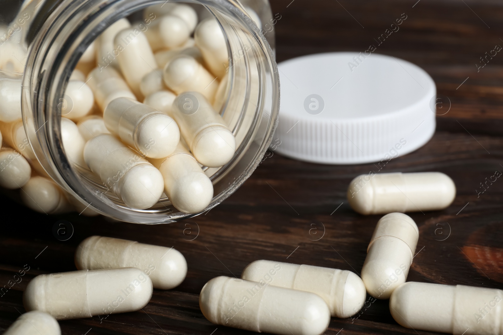 Photo of Glass medical bottle and pills on wooden table, closeup