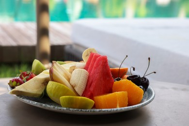 Photo of Plate with fresh fruits on table near sun lounger. Luxury resort with outdoor swimming pool