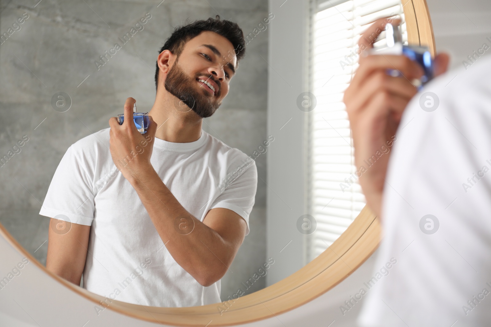 Photo of Man spraying luxury perfume near mirror indoors