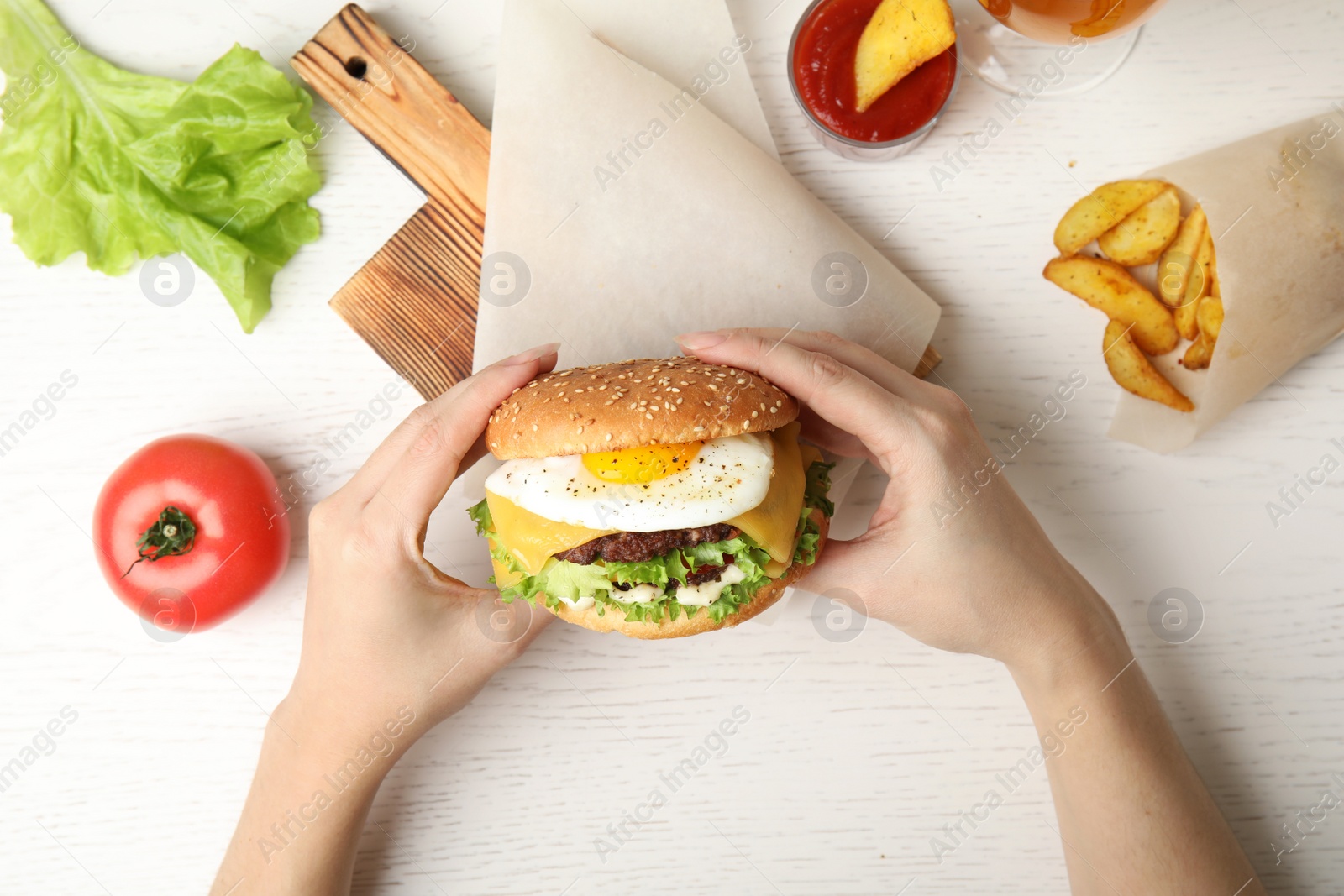 Photo of Woman holding tasty burger with fried egg over table, top view