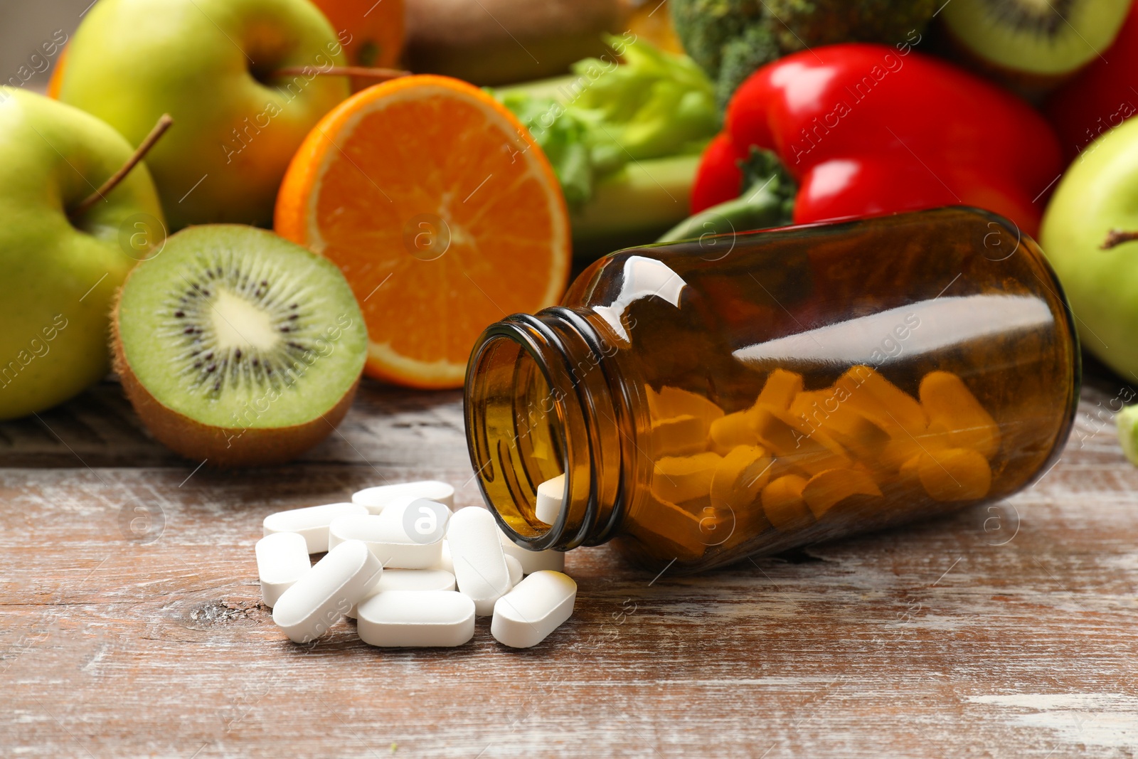 Photo of Dietary supplements. Overturned bottle, pills and food products on wooden table, closeup