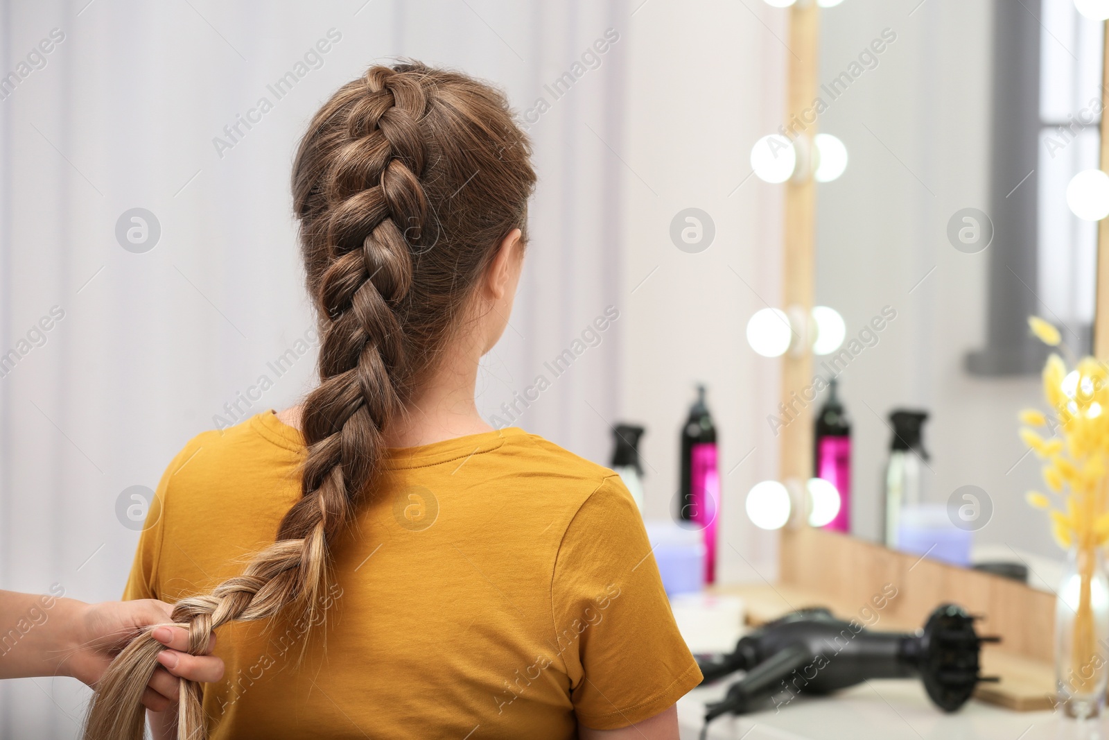 Photo of Professional coiffeuse braiding client's hair in salon