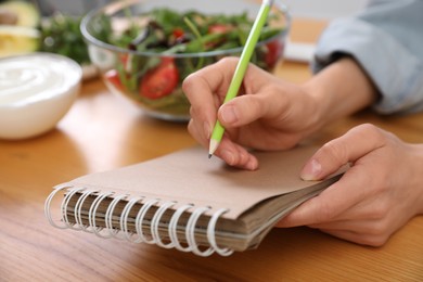 Woman with notebook at wooden table, closeup. Keto diet