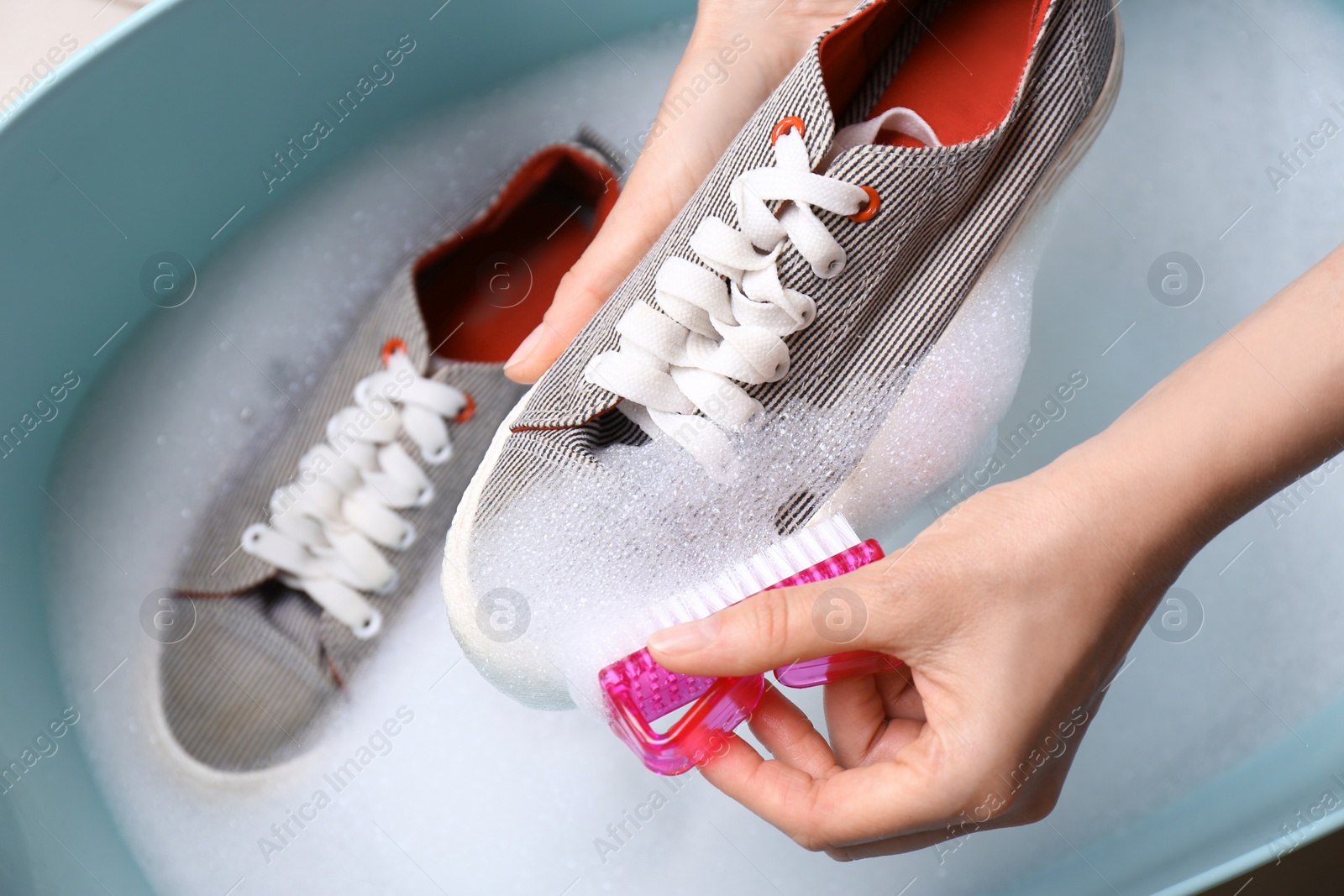 Photo of Woman washing shoe with brush in basin, closeup