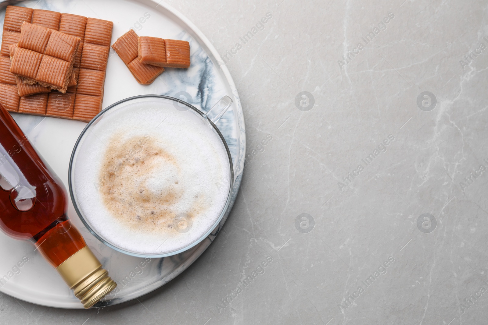 Photo of Bottle of delicious syrup, glass of coffee and caramel candies on grey table, top view. Space for text