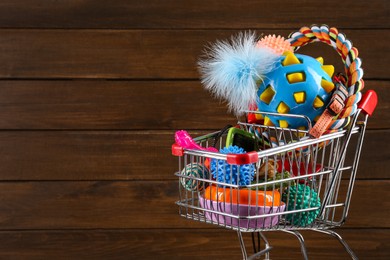 Photo of Shopping cart with different pet shop goods on wooden background, space for text
