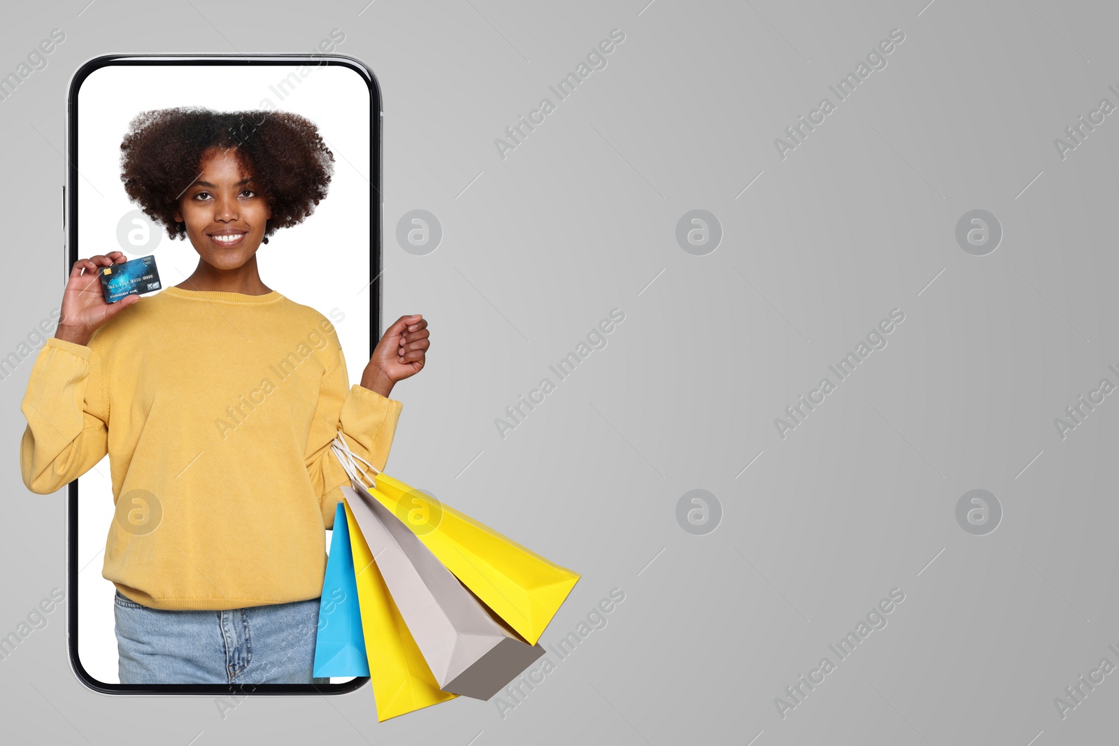 Image of Online shopping. Happy woman with paper bags and credit card looking out from smartphone on gray background, space for text