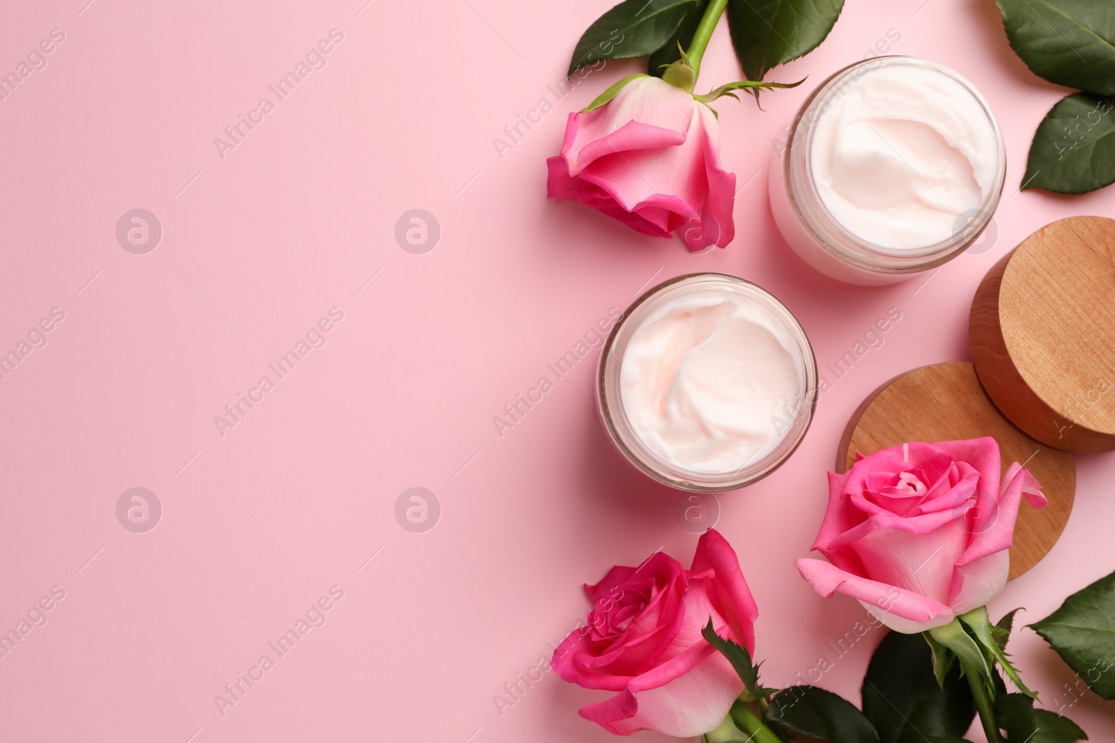 Photo of Glass jars of face cream and roses on pink background, flat lay. Space for text