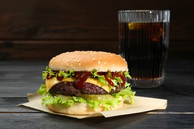 Photo of Burger with delicious patty and soda drink on black wooden table