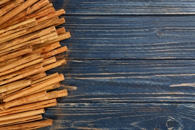 Photo of Aromatic cinnamon sticks on blue wooden table, flat lay. Space for text