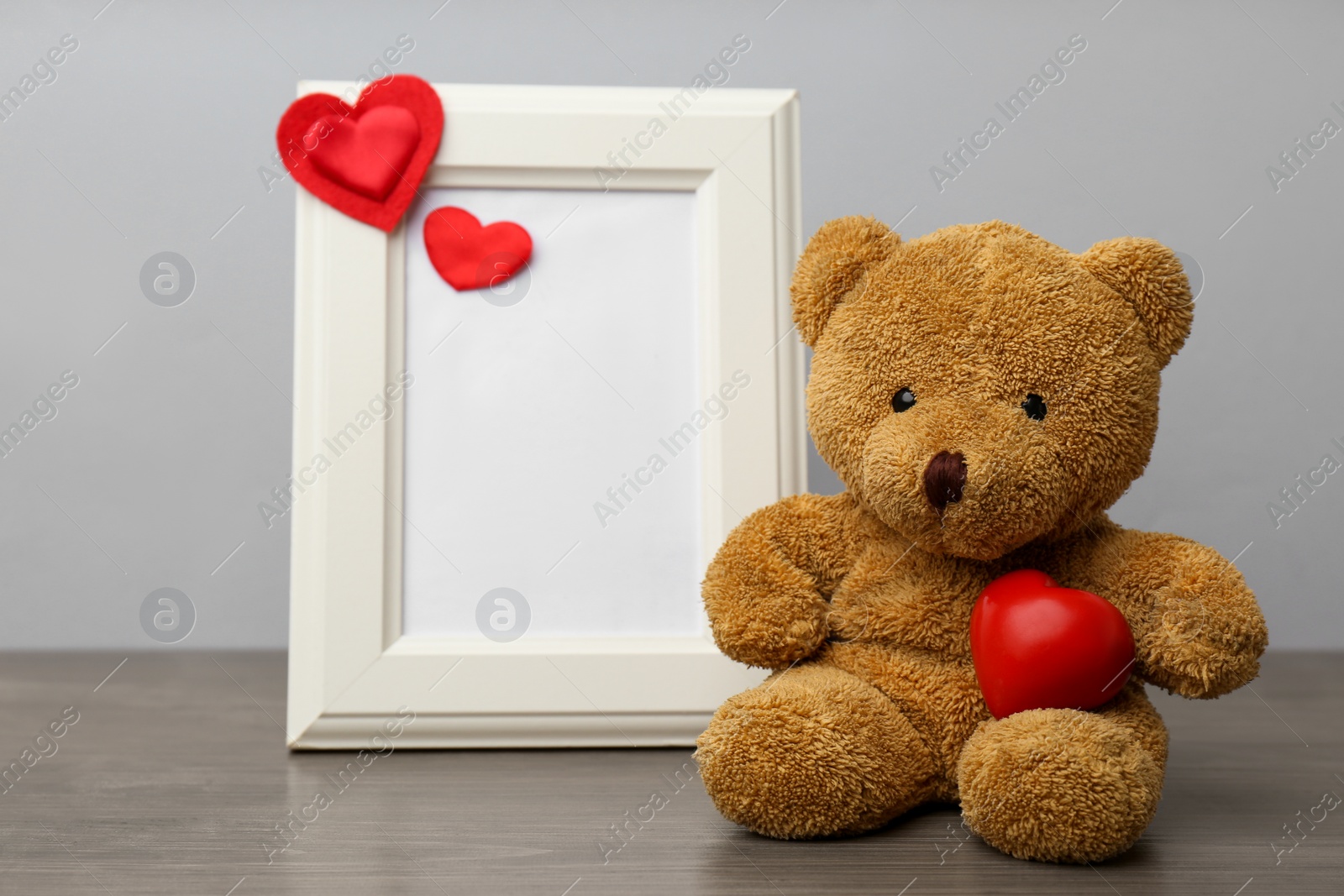 Photo of Cute teddy bear with red heart and frame on wooden table. Valentine's day celebration