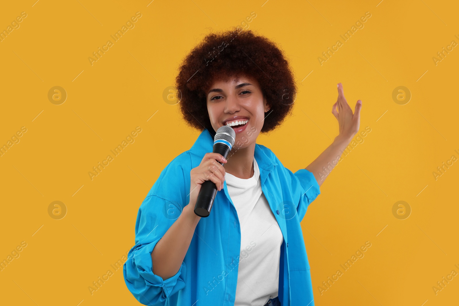 Photo of Curly young woman with microphone singing on yellow background