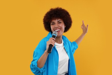 Curly young woman with microphone singing on yellow background