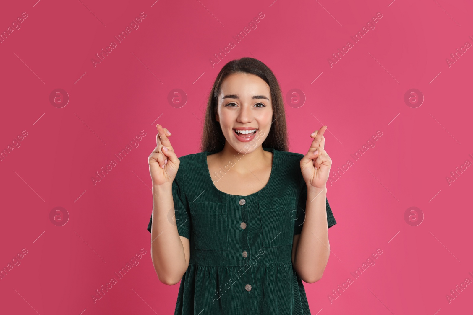 Photo of Woman with crossed fingers on pink background. Superstition concept