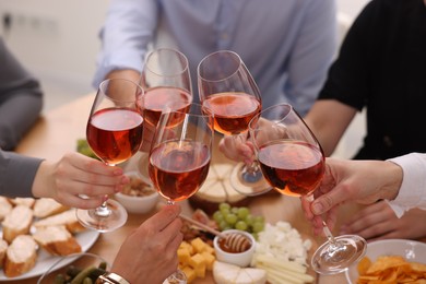 Photo of People clinking glasses with rose wine above table indoors, closeup